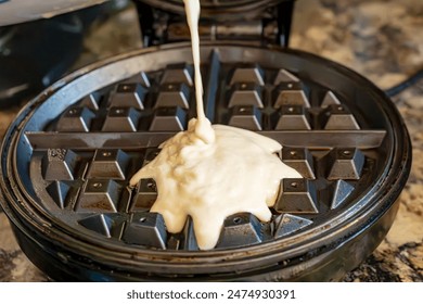 Adding waffle batter to a hot round electric waffle maker.