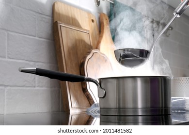 Adding water with ladle into steaming saucepan on stove in kitchen