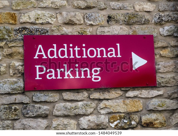 Additional Parking sign. White writing on red\
background. Sign attached to rustic brick wall. Concept of parking\
problems and too many\
cars.