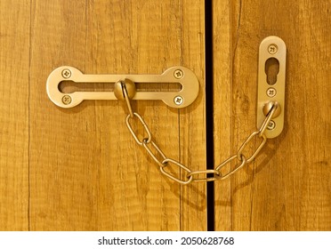 Additional security lock with chain and sliding on wooden door.