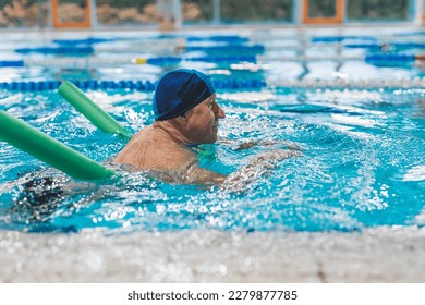 Additional swimming equipment. Side view of an elderly white man in a swimming cup, using green pool noodle. Active seniors. High quality photo