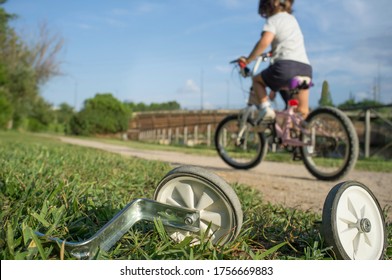 Additional Wheels Lying On The Grass While A Boy Begins To Ride Without Them. First Day Without Training Wheels Concept