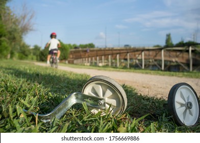 Additional Wheels Lying On The Grass While A Boy Begins To Ride Without Them. First Day Without Training Wheels Concept