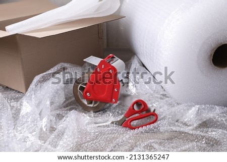 Adhesive tape with bubble wrap, scissors and cardboard box on table