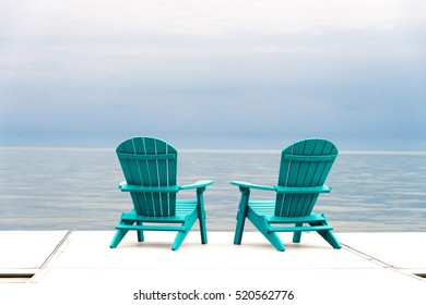 Adirondack Chairs at the end of a pier overlooking a large blue lake with a blue sky 