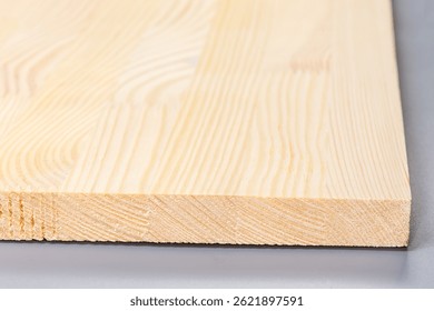 Adjacent ends of the flat wood panel made from the light colored pine planks glued together, side view close-up in selective focus on a gray background 