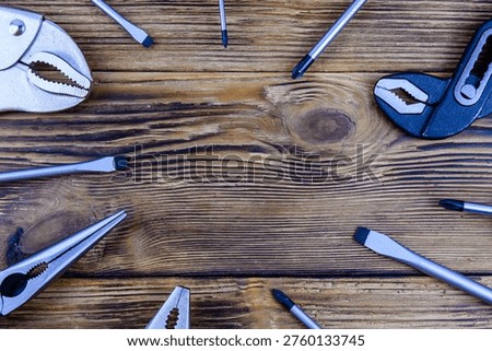 Adjustable water pump pliers, needle nose pliers locking pliers and screwdrivers on wooden background. Top view