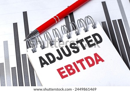 ADJUSTED EBITDA text on a notebook on chart with pen . 
