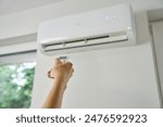 Adjusting air conditioner temperature with remote control. Hand holds remote control and setting comfortable temperature on climate system in apartment