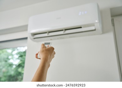 Adjusting air conditioner temperature with remote control. Hand holds remote control and setting comfortable temperature on climate system in apartment