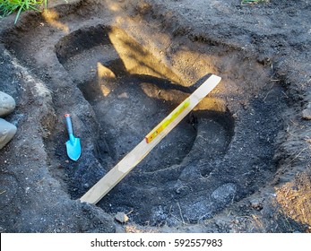 Adjusting horizontal plane with a bubble level and trowel of a dug stepped hole prepared for installation of a preformed plastic pond insert in the summer garden