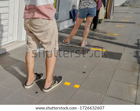 Adjusting to the new normal by practicing social distancing in daily life. Customers queuing up 1 meter apart based on sticker before entering a shop. 