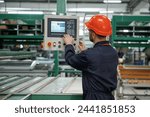 Adjusting settings of machine, operating. Factory worker is indoors with hard hat.