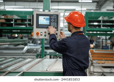 Adjusting settings of machine, operating. Factory worker is indoors with hard hat.