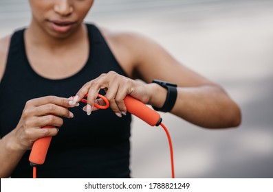 Adjustment of sports equipment. Serious african american girl in sportswear with fitness tracker adjusts skipping rope for workout, cropped, close up, free space - Powered by Shutterstock