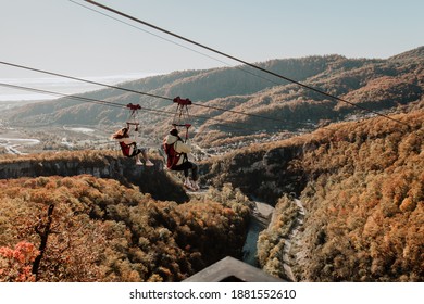 Adler. Sochi park. Two girls tourists ride a zipline against the background of an autumn forest and mountains. - Powered by Shutterstock