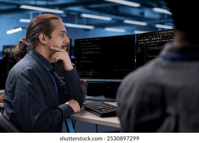 Admin in data center updating systems, protecting hardware equipment from damaging software vulnerabilities. Colleagues looking for bugs causing infrastructure to slow down