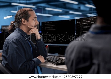 Admin in data center updating systems, protecting hardware equipment from damaging software vulnerabilities. Colleagues looking for bugs causing infrastructure to slow down