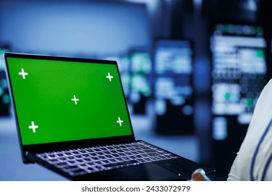 Admin in data center uses mockup laptop to prevent server machines overload. Expert between server mainframes using isolated screen device to ensure enough network bandwidth for smooth operations