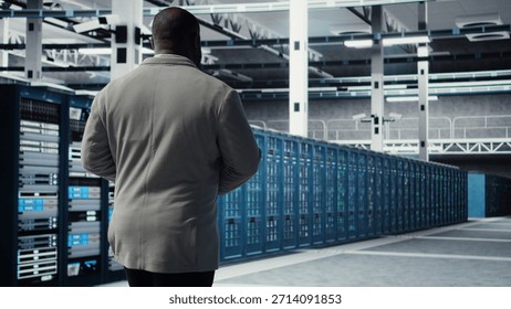 Admin walking in data center, doing inspection on infrastructure tech handling user requests. IT professional in server farm analyzing traffic patterns of equipment components, camera A