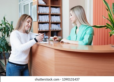 Administrator And Patient At The Reception In The Medical Office. Young Female Receptionist With Client In Hospital.