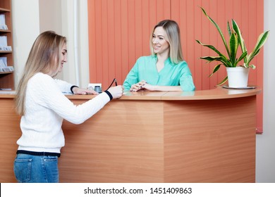 Administrator And Patient At The Reception In The Medical Office. Young Female Receptionist With Client In Hospital.