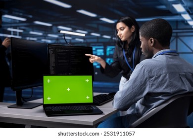 Admins using mockup laptop to reconfigure server room facility, optimizing it for data processing requirements. Workers using green screen notebook, ensuring data center tech operates efficiently
