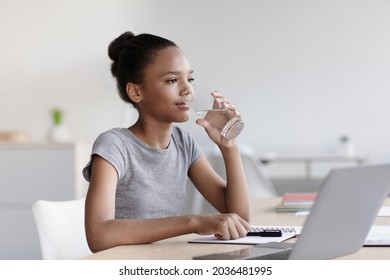 Adolescent African American Girl Drinks Water From Glass And Studies With Laptop In Living Room Interior. Health Care, Aqua Balance, Home Education, Remote Lesson During Covid-19 Outbreak, Copy Space