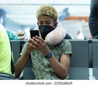 Adolescent Afro Latino Sit At The Airport With Mobil Phone