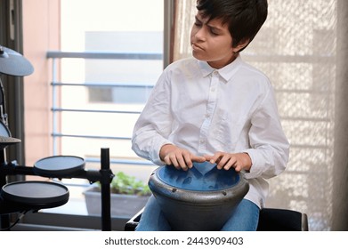 Adolescent boy musician enjoying playing the African ethnic percussion musical instrument drum - djembe, bongo, tam tam. Happy teenager creating the rhythm of African music banging ethnic drum - Powered by Shutterstock