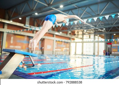 Adolescent Boy In Swimwear Doing Jump Into Water Of Swimming-pool From Diving Board