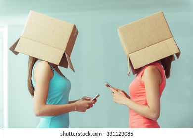 Adolescent girls with boxes on their heads texting with their smart phones, social networks and isolation concept