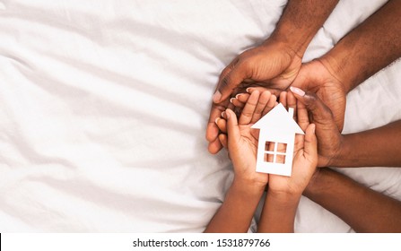 Adoption concept. Black family of three holding paper house figure in hands over white bed sheet background, panorama with free space - Powered by Shutterstock