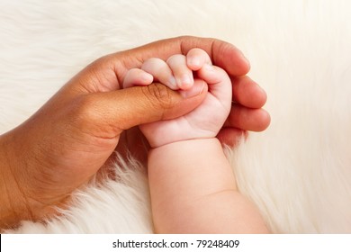 Adoption Concept Where Dark Skin Parent Holding Hand Of Asian Baby