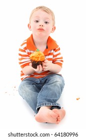 Adorable 2 year old toddler boy with orange frosting cupcake over white background.