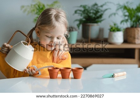 Adorable 3 years old caucasian blonde little girl is watering new plants in the pots at home. concept of plant growing learning activity for preschool kid and child education. Earth Day. 