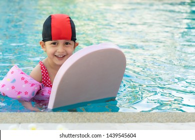 Adorable 3 Years Old Girl Is Floating In The Swimming Pool With Big Smiley Face For Her Experience To Learn About Swiming, Concept Of Sport And Outdoor Activity For Kid Devepment.