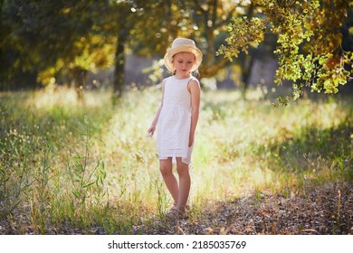 Adorable 4 Year Old Girl In White Dress And Straw Hat Walking In A Garden In Provence, France