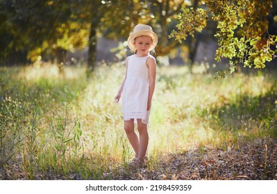 Adorable 4 Year Old Girl In White Dress And Straw Hat Walking In A Garden In Provence, France