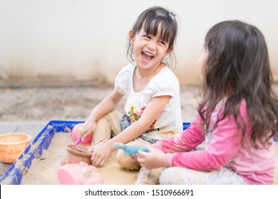 Adorable 4 Years Old Asian Little Girl Is Playing The Sand Mud With Her Unidentified Friend With Fully Happiness Moment, Concept Of Outdoor Freeplay For Kid Development And Social Skill For Childhood.