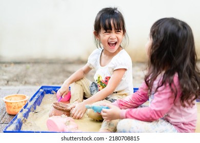 Adorable 4 years old asian little girl is playing the sand mud with her unidentified friend with fully happiness moment, concept of outdoor freeplay for kid development and social skill for childhood. - Shutterstock ID 2180708815