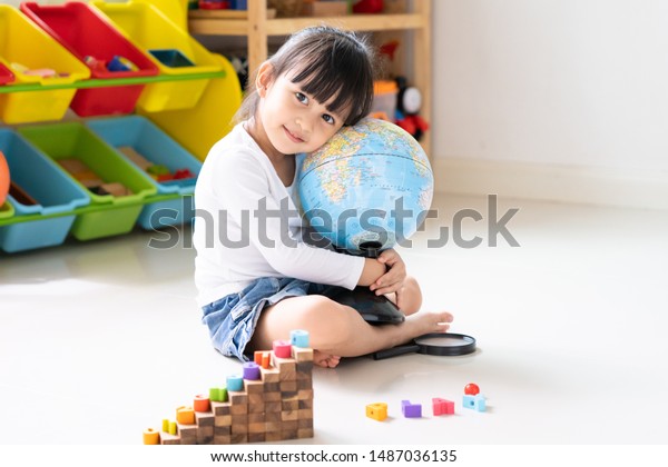 Adorable 4 years old asian little girl is hugging\
the bilingual globe model contain english and thai language,\
concept of save the world and learn through play activity for kid\
education at home.