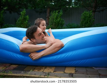 Adorable 5 Years Old Little Girl Hugging Her Loving Dad While Lying On His Back, Having Fun Together In The Inflatable Pool At Home Backyard Garden. Father And Daughter. Family Relationships Concept