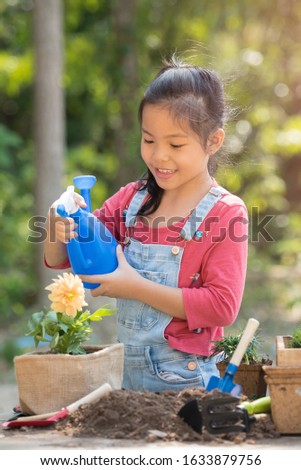 adorable 8 years old asian little girl is watering plant in pots in garden outside house, child education of nature. caring for a new life. earth day holiday concept. world environment day. ecology.