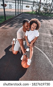 Adorable African American Kid Laughing While Standing On A Basketball Court With His Smiling Dad