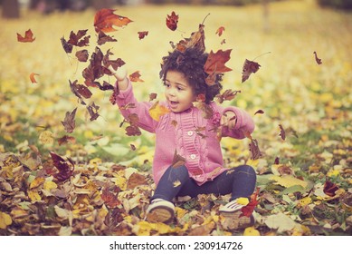 Adorable african american mixed race kid wearing casual clothes playing in park with bunch of leaves, enjoying warm autumn day - Powered by Shutterstock