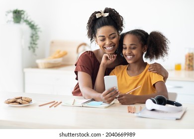 Adorable african american mother and daughter sitting at kitchen table taking selfie together while spending time together, happy black mom and kid having video chat, using cellphone, copy space - Powered by Shutterstock