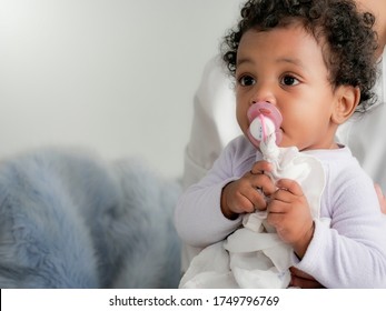 An adorable African baby boy or toddler with pacifier or dummy in his mouth. Cute infant feel napping with dummy in mom's arms