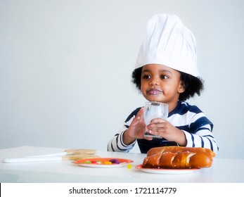 An adorable African boy role play like a chef and drinking a cup of milk in the kitchen.