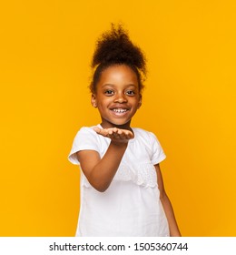 Adorable african little girl sending air kiss to camera, orange studio background